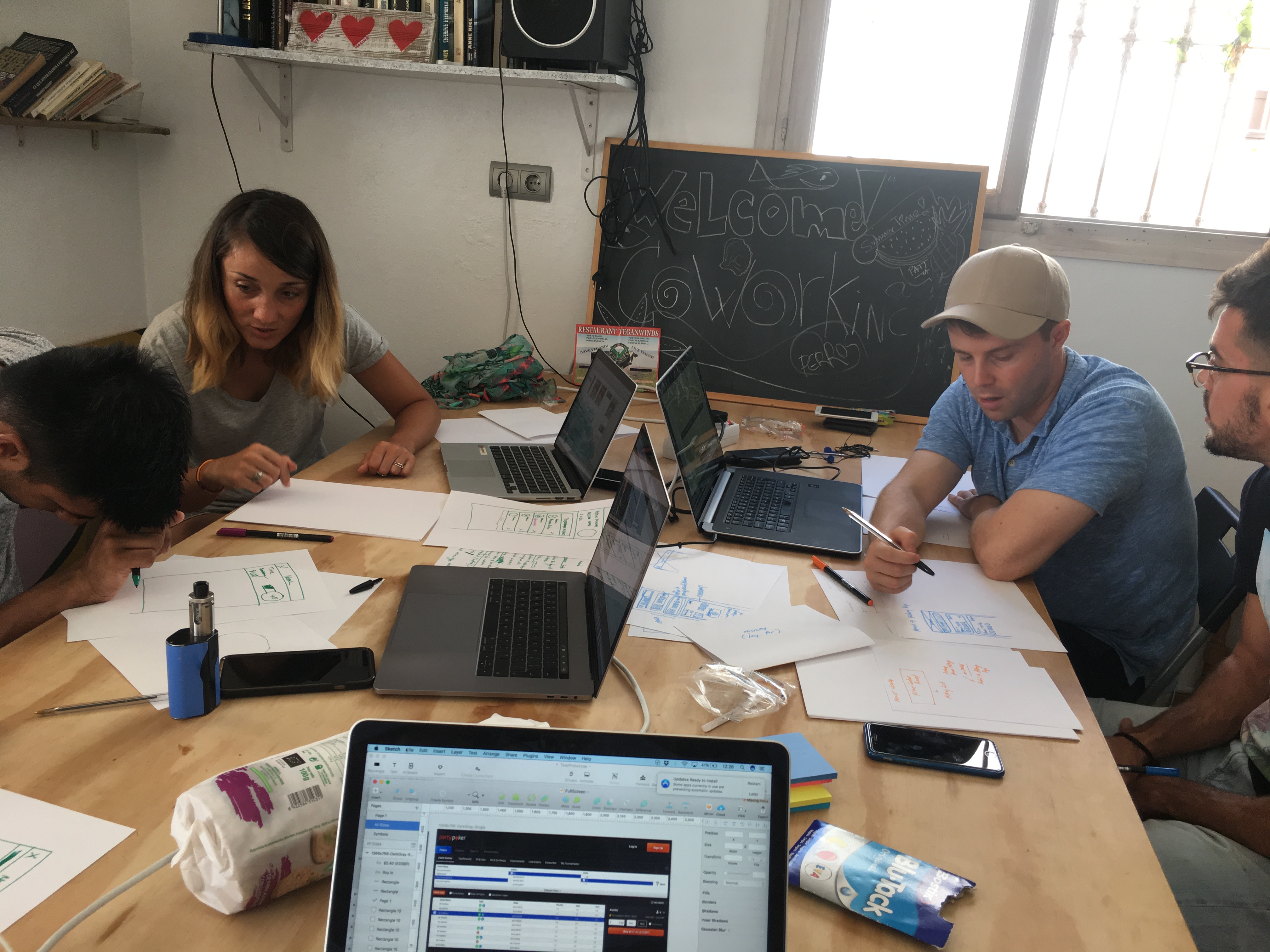 The cashier project team in the first Tarifa workshop. Laptops out, sketches on paper, the chalkboard reading 'Welcome Coworking' on the back wall.